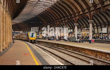 Ein Bahnhof mit einem Zug, der auf die Abfahrt wartet. Ein aus Metall und Glas gedachtes Baldachin aus dem 19th. Jahrhundert mit Säulen steht über dem Kopf und die Passagiere warten auf Züge. Stockfoto