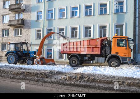 KRONSHTADT, RUSSLAND - 18. JANUAR 2022: Traktor 'Belarus' und Muldenkipper 'Mercedes Benz' reinigen den Bürgersteig auf der Stadtstraße von Schnee Stockfoto