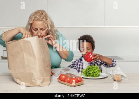Mutter und Sohn nehmen Lebensmittel aus der Papiertasche. Lieferung von Lebensmitteln Stockfoto