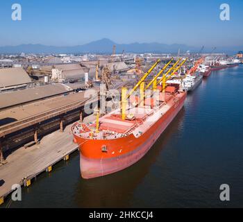 Drohne Luftaufnahme des roten Massengutfrachtschiffes mit Soja am Seehafen am sonnigen Sommertag beladen. Konzept von Logistik, Handel, Wirtschaft, Industrie. Stockfoto