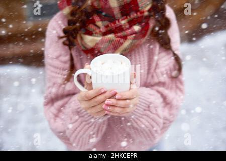 Junge Frau hält Tasse heiße Schokolade mit Marshallows im Freien am Wintertag Stockfoto