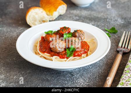 Spaghetti mit Fleischbällchen und Tomatensauce auf einem weißen Teller auf grauem Grund. Stockfoto