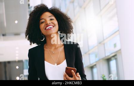 Es ist wie mein eigener tragbarer persönlicher Assistent. Aufnahme einer jungen Geschäftsfrau, die ein Smartphone benutzt, während sie durch ein modernes Büro geht. Stockfoto