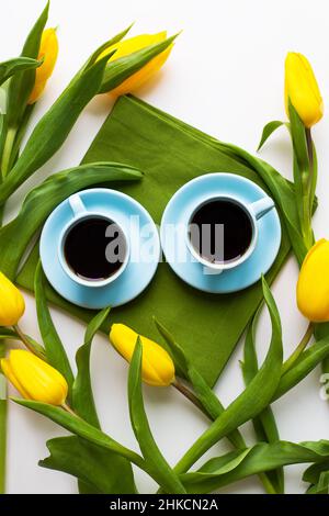 Zwei blaue Tassen Kaffee auf einem Tisch mit grünem Tuch und gelbe Tulpen Stockfoto