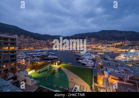 Luftaufnahme des Hafens Hercules in Monaco - Monte-Carlo in der Abenddämmerung liegen viele Yachten und Boote in der Marina, Stadtbild mit Nachtbeleuchtung, Magie Stockfoto