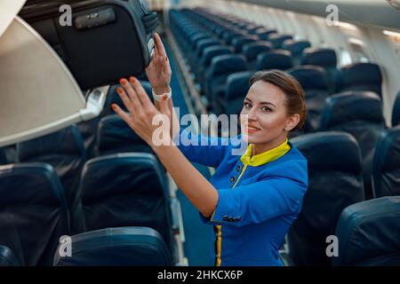 Stewardess: Reisetasche im Gepäckregal über dem Kopf im Flugzeug Stockfoto