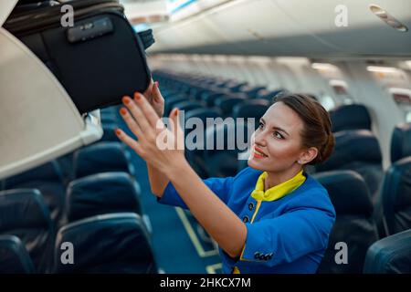 Fluggastgeberin, die Reisetasche im Flugzeug in den Gepäckraum über dem Kopf legt Stockfoto