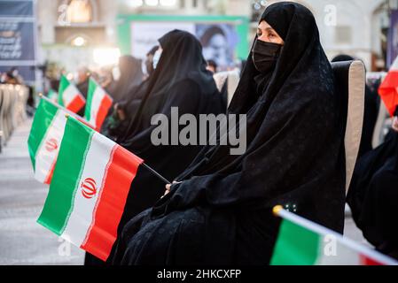 Teheran, Iran. 01st. Februar 2022. Eine verschleierte Frau, die eine Schutzmaske trägt, hält eine iranische Flagge, während sie am 1. Februar vor dem Grab des verstorbenen iranischen Führers Ayatollah Ruhollah Khomeini am ersten Tag des Sieges des Jahrestages der Islamischen Revolution auf dem Friedhof Behesht-e Zahra im Süden Teherans, Iran, sitzt. 2022. (Foto: Sobhan Farajvan/Pacific Press/Sipa USA) Quelle: SIPA USA/Alamy Live News Stockfoto