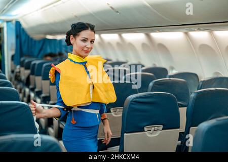 Stewardess demonstriert, wie man Rettungsweste im Flugzeug verwendet Stockfoto