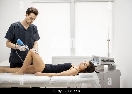 Der Arzt wendet eine Schockwellentherapie auf das Knie der Frau an Stockfoto