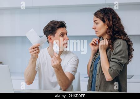 Junger Mann und Frau diskutieren Geldsummen im Supermarkt Scheck und streiten über Ausgaben am Tisch mit Laptop und Rechner in der Küche Stockfoto