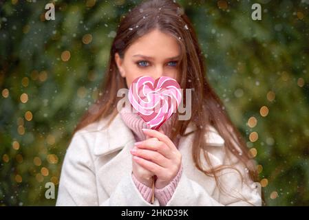 Mädchen verstecken Mund von süßen Süßigkeiten. Herzförmige Karamell Süßigkeiten in der Hand des Mädchens. valentinstag Konzept Stockfoto