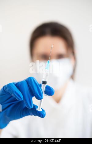 Junger Arzt mit einer Spritze in den Händen. Arzt in Innenräumen macht Impfungen. Eine Frau in einem medizinischen Büro. Impfung gegen Influenza und Viren Stockfoto
