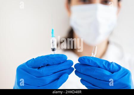 Ein junger Arzt mit einer Spritze und einem Impfstoff in den Händen. Arzt in Innenräumen macht Impfungen. Eine Frau in einem medizinischen Büro. Impfung gegen Influenza Stockfoto