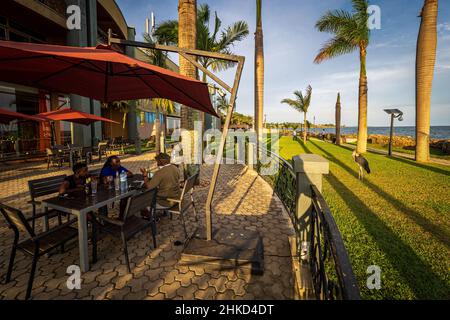 Ein Marabou stielt an Menschen vorbei, die auf der Terrasse eines gehobenen Restaurants am Ufer des Victoriasees, Entebbe, Uganda, sitzen Stockfoto