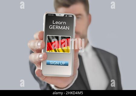 Online-Konzept Lernen Sie die deutsche Sprache mit einer Person, die E-Learning-App auf dem Handy zeigt, wobei die Flagge Deutschlands isoliert ist Stockfoto