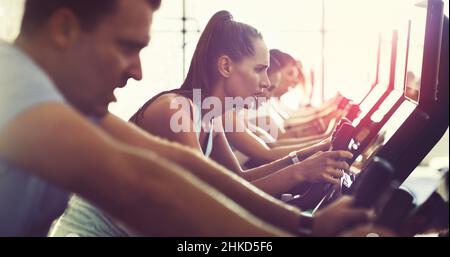 Intensiviert ihr Training. Eine kurze Aufnahme einer Gruppe junger Menschen, die im Fitnessstudio an elliptischen Geräten trainieren. Stockfoto