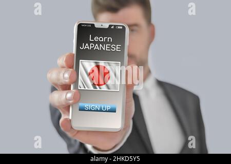Online-Konzept Lernen Sie die japanische Sprache mit einer Person, die E-Learning-App auf dem Mobiltelefon zeigt, wobei die Flagge Japans isoliert ist Stockfoto