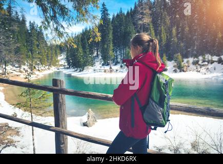 Junge Frau mit Rucksack steht in der Nähe des Sees mit blauem Wasser Stockfoto