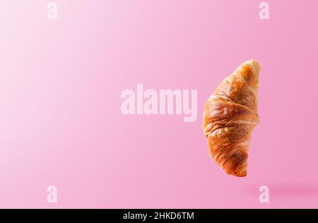 Frisch gebackene Croissants schweben oder fliegen. Croissant fliegen in der Luft isoliert auf rosa Hintergrund. Levitation-Szene. Platz kopieren. Schildermockup oder Werbung für Bäckerei, Süßwaren Stockfoto