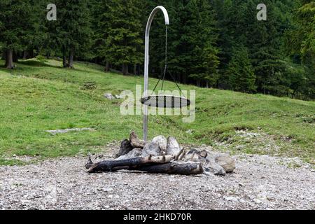 Leerer Kamin mit schwarzem Metallgitter Rost auf großem Schotterplatz, verkohltes Holz zwischen großen Steinen, grüner Tannenwald im Hintergrund tagsüber wit Stockfoto