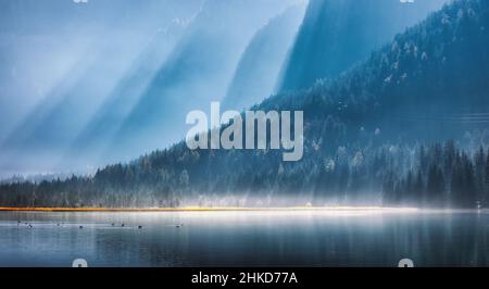 Berge in hellen Sonnenstrahlen und nebliger See am sonnigen Morgen Stockfoto