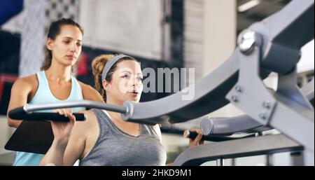 Fangen wir an Eine kurze Aufnahme einer weiblichen Fitnesstrainerin, die ihre Klientin durch ein Workout im Fitnessstudio führt. Stockfoto