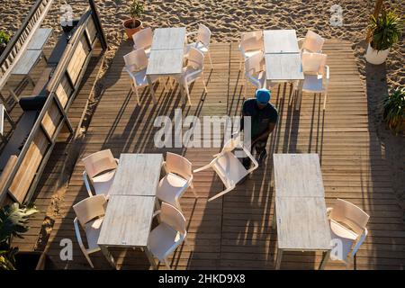 Spanien. 29th Januar 2022. Am frühen Morgen wird in einem Strandrestaurant am Strand von Barceloneta in Barcelona, Spanien, am 29. Januar 2022 ein schwarzer Mann gesehen, der Stühle und Tische für den Tag vorbereitet. (Foto von Davide Bonaldo/Sipa USA) Quelle: SIPA USA/Alamy Live News Stockfoto