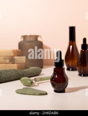 Spray- und Tropfflaschen aus Bernstein-Glas mit Kosmetik auf hellem Badezimmertisch. Natürliche Jade Roller für Gesichtsmassage und Guasha Massage Board. Stockfoto