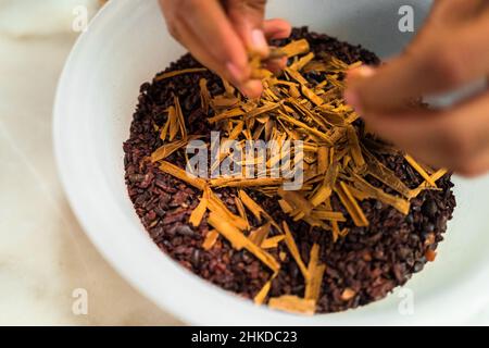 Ein mexikanischer Mann fügt Zimt in zerkleinerte Kakaobohnen vor dem Mahlprozess in der handwerklichen Schokoladenherstellung in Xochistlahuaca, Mexiko, hinzu. Stockfoto