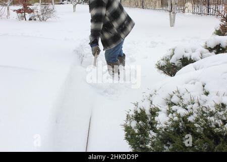 Ein Mann räumt Schnee aus einem Außenpool in einem privaten Hof. Wasserbecken Wartung im Winter. Stockfoto