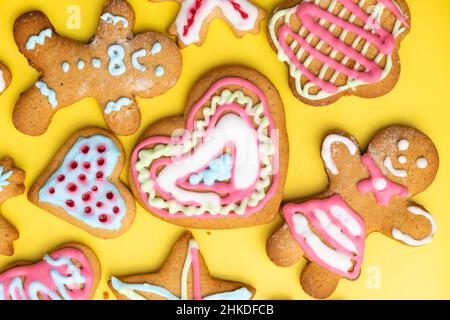 Herzförmige Zuckerkekse und Junge und Mädchen Lebkuchen für den Valentinstag mit buntem Glasur auf dem gelben Hintergrund. Stockfoto