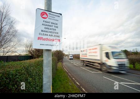 Nutzfahrzeuge fahren im Großraum Manchester an einem Schild der Clean Air Zone vorbei, das aus Protest gegen das Vorhaben von einem Plakat verdeckt wird Stockfoto