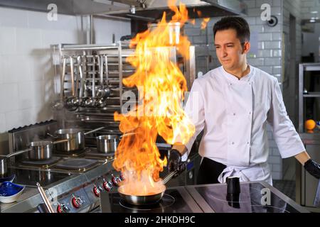 Nahaufnahme der Hände des Küchenchefs, die Speisen auf Feuer kochen. Der Koch verbrennt Essen in einer professionellen Küche Stockfoto