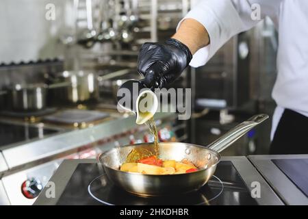 Nahaufnahme der Hände des Küchenchefs, die Speisen auf Feuer kochen. Der Koch verbrennt Essen in einer professionellen Küche Stockfoto