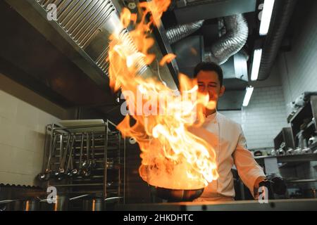 Nahaufnahme der Hände des Küchenchefs, die Speisen auf Feuer kochen. Der Koch verbrennt Essen in einer professionellen Küche Stockfoto