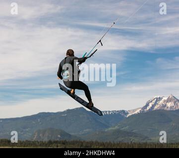 Kite Surfer fliegt über den Himmel, Berge. Kitesurfer springt an einem sonnigen Sommertag über das Wasser. Mann Hobbys und Erholung Kitesurfen, Kiteboarding-Ju Stockfoto