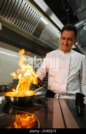 Nahaufnahme der Hände des Küchenchefs, die Speisen auf Feuer kochen. Der Koch verbrennt Essen in einer professionellen Küche Stockfoto