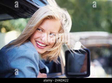 Luftig. Eine junge Frau spürt die Brise in ihren Haaren durch ein offenes Autofenster. Stockfoto