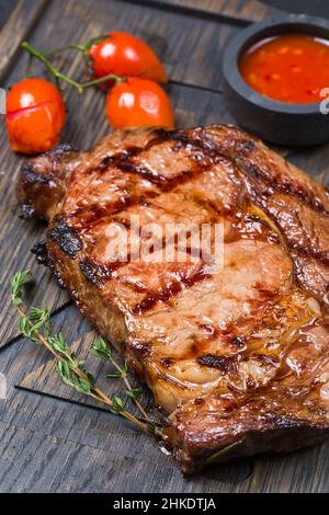 Gebratenes Rib Eye Steak mit Kirschtomaten und Sauce auf einem Holzbrett Stockfoto