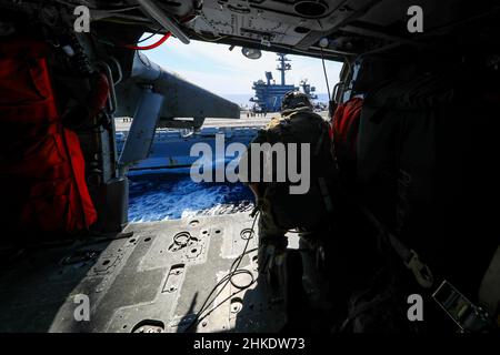 SÜDCHINESISCHES MEER (FEB 1, 2022) Senior Chief Naval Aircrewman (Hubschrauber) Justin Wright aus Linden, Kalifornien, beobachtet den Flugzeugträger USS Abraham Lincoln (CVN 72) der Nimitz-Klasse aus der Kabine eines Hubschraubers MH-60s Sea Hawk, der den 'Chargers' des Helicopter Sea Combat Squadron (HSC) 14 zugewiesen wurde. Die Abraham Lincoln Strike Group befindet sich im geplanten Einsatzgebiet der US-Flotte für 7th, um die Interoperabilität durch Allianzen und Partnerschaften zu verbessern und gleichzeitig als reaktionsfähige Truppe zur Unterstützung einer freien und offenen Region im Indo-Pazifik-Raum zu dienen. (USA Navy Foto von Mass Communication Specia Stockfoto