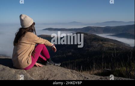 Weibchen sitzt auf einem Felsen auf dem Gipfel von Malinowska Skala und blickt auf die nebligen Berge Stockfoto