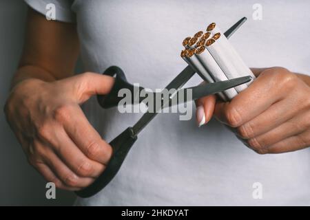 Frau schneidet mit einer Schere Zigaretten. Hören Sie auf zu rauchen, hören Sie auf zu rauchen oder rauchen Sie nicht. Frau, die Tabak ablehnt. Beende schlechte Angewohnheit Stockfoto