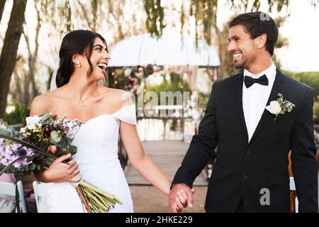 Jung, frei und verliebt. Aufnahme eines glücklichen jungen Ehepaares, das an ihrem Hochzeitstag die Hände im Freien zusammenhält. Stockfoto