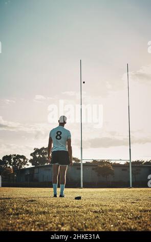 Und der Ball geht weiter. Rückansicht eines hübschen jungen Rugby-Spielers, der tagsüber auf dem Spielfeld tritt. Stockfoto