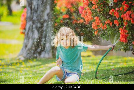 Glücklicher Junge gießt Wasser aus einem Schlauch. Kinder bewässern Blumen im Garten. Gartenarbeit im Haus. Stockfoto