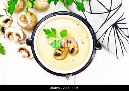 Suppenpüree aus Champignons, Kartoffeln, Zwiebeln und Rahm in einer Schüssel, Küchentuch, Petersilie und Löffel auf Holzbrett Hintergrund von oben Stockfoto