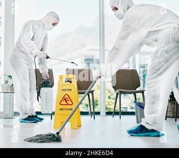 Korona kontrollieren und sauber halten. Aufnahme von Mitarbeitern im Gesundheitswesen, die während eines Ausbruchs Gefahrgutanzüge tragen und einen Raum desinfizieren. Stockfoto