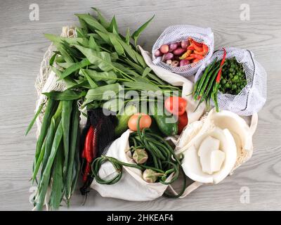 Frisches Gemüse in Öko-Baumwollbeuteln auf dem Tisch in der Küche. Kangkung, Chili, Long Bean, Tomate, Kokosnuss, Frühlingszwiebeln, Ei, Gurke, Aubergine aus Stockfoto