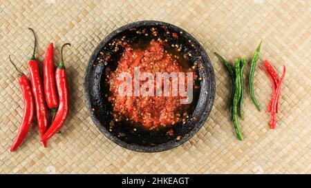 Chilipaste oder Sambal, Draufsicht mit rotem Chilischoten auf gewebter Matte. Konzept Spicy Food Stockfoto